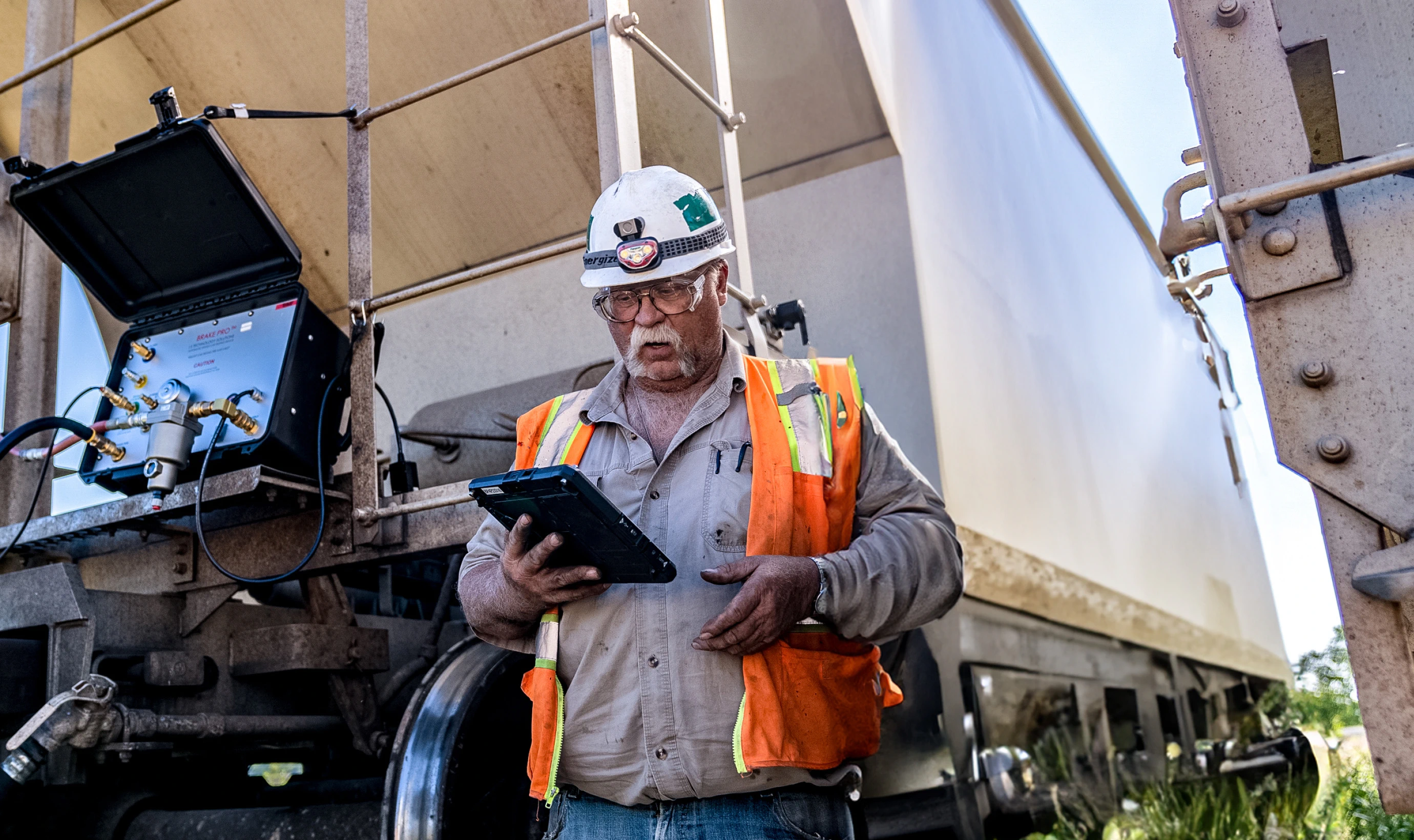 pattison Sand worker in hardhat standing in front of railcar looking at tablet